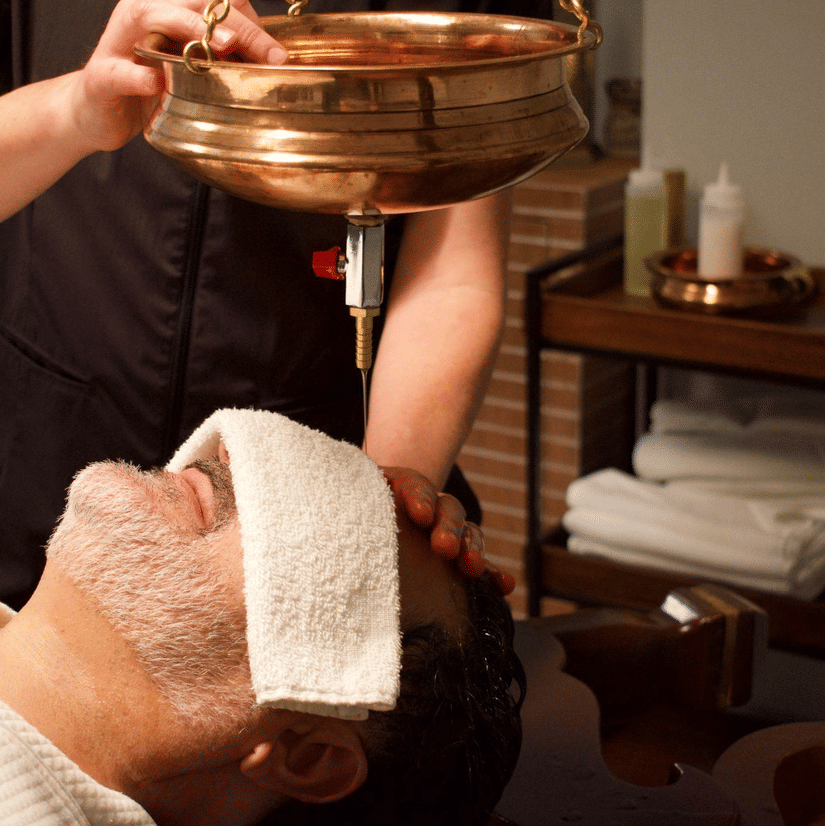 A person receives a traditional Ayurvedic oil therapy with a cloth over their eyes in a serene spa treatment room