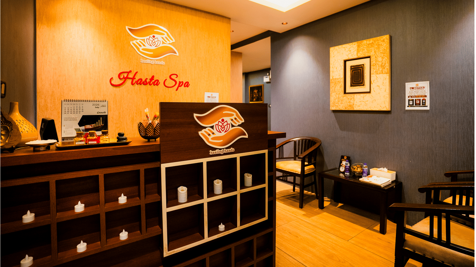 Hasta Spa reception with the healing hands logo on a timber wall, oil bottles on the counter and waiting chairs at Ilara Hotels & Spa, Tada.