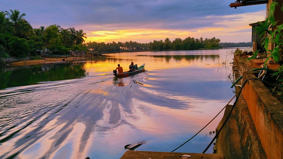 A sunset view of a calm river with two people kayaking surrounded by greenery at Paradise Lagoon Resort, Udupi.