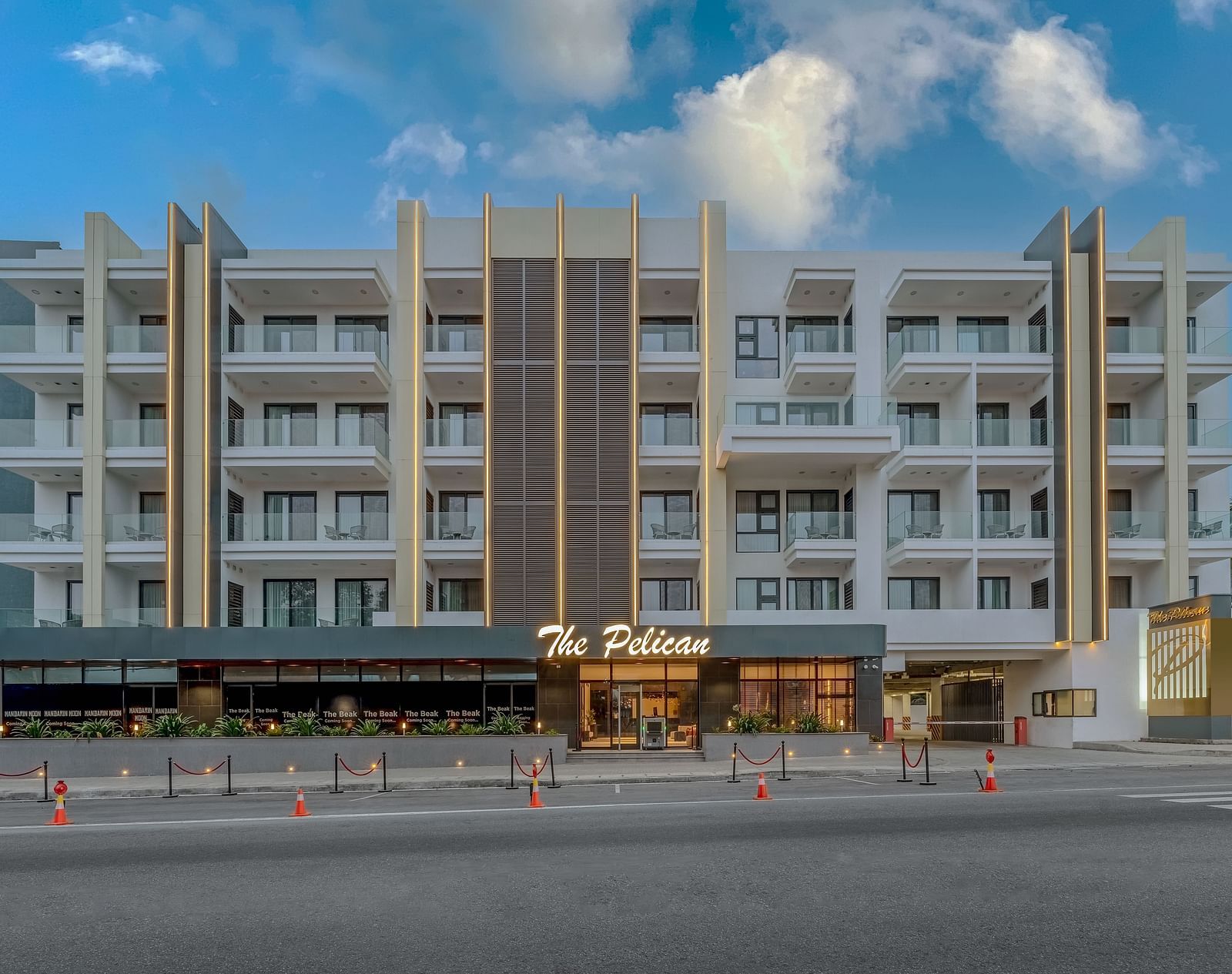 A tall white hotel building with palm trees in front and a clear blue sky in the background - The Pelican Hotel, Accra - Accra Hotel Images.