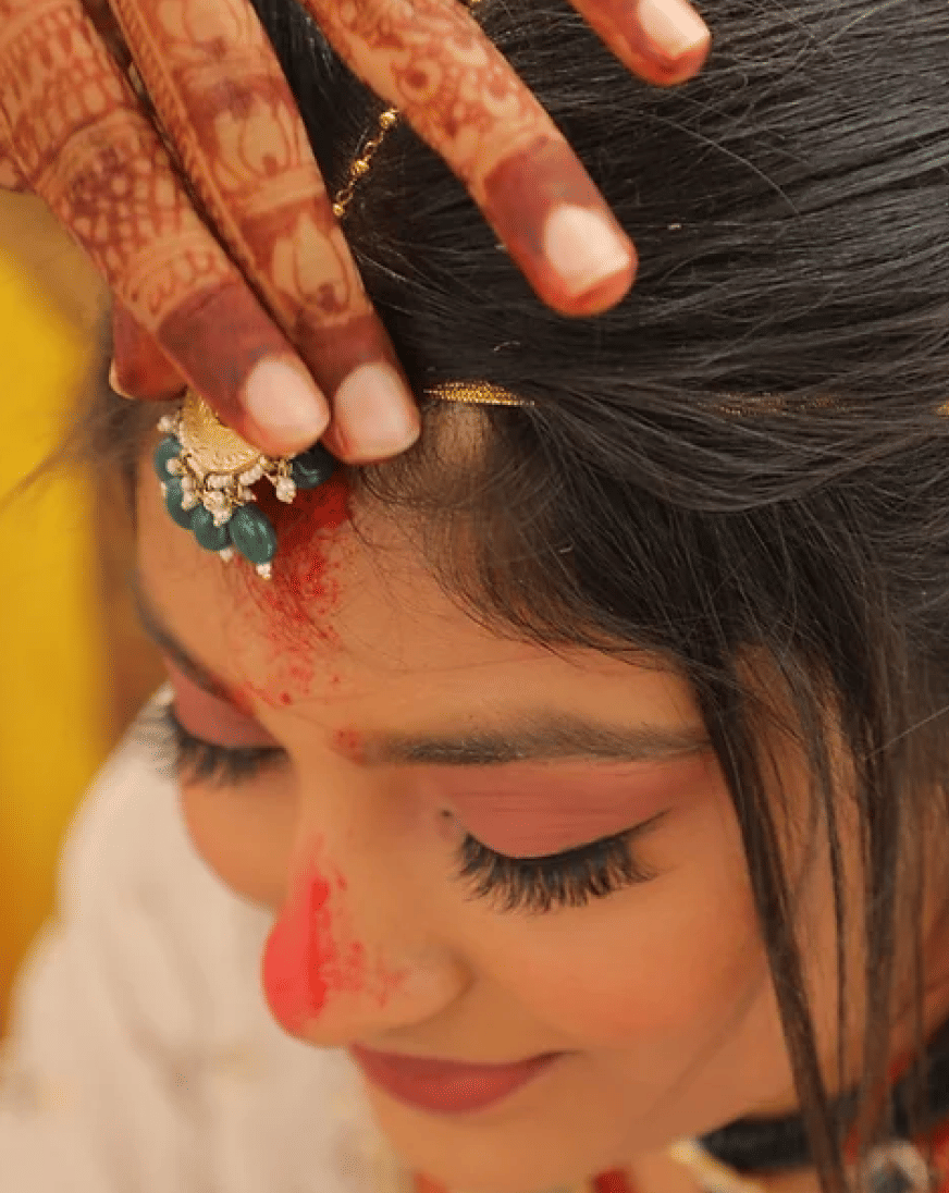 Image of a woman having her maang tikka adjusted.
