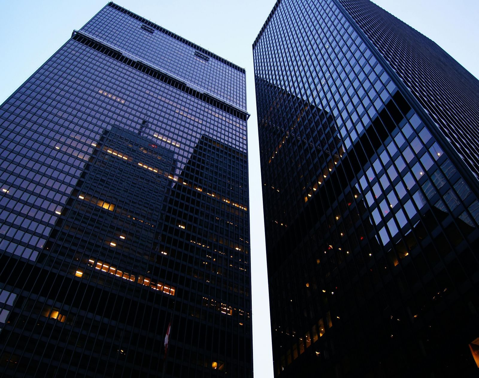 Two tall, dark skyscrapers against a clear, bright sky.