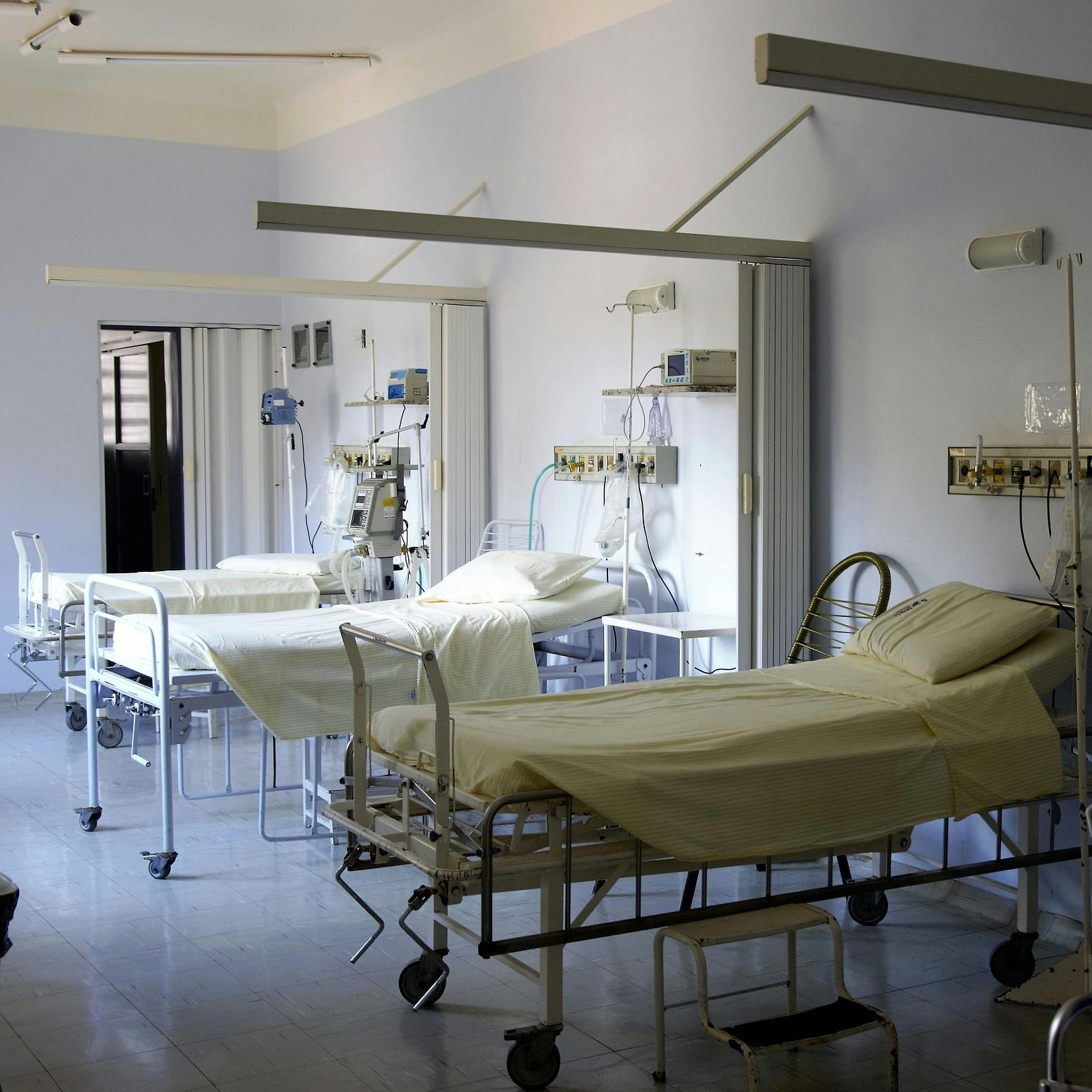 Interior of a hospital room with three beds, chairs, and medical devices.