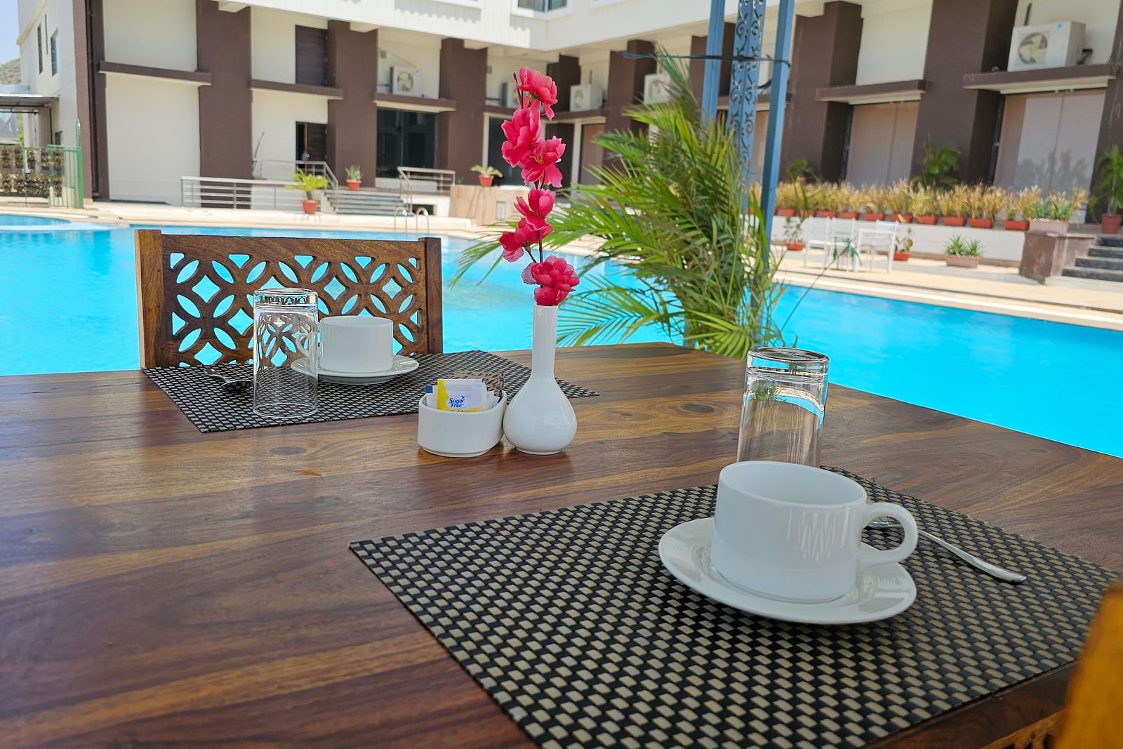 An outdoor dining table set for two beside a bright blue swimming pool - Bamboo Saa Mulberry Resort, Pushkar