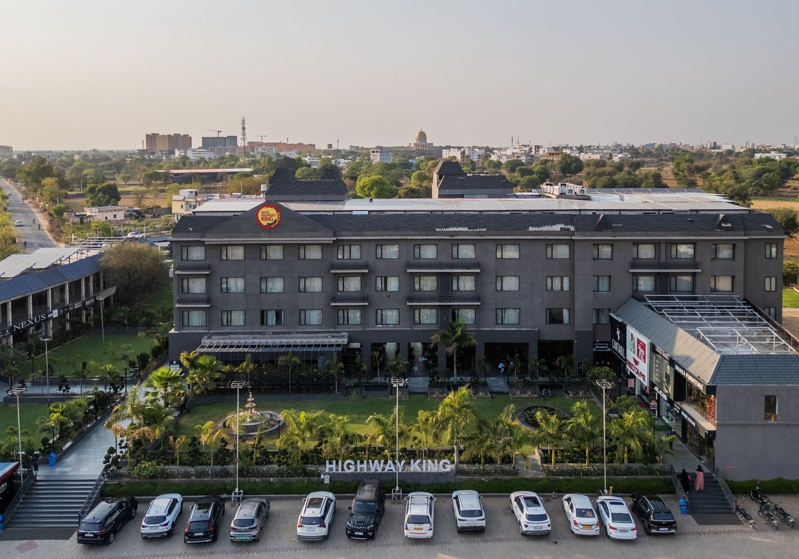 Aerial view of Hotel Highway King, Bagru, with landscaped gardens, parking area, and surrounding buildings in the background.