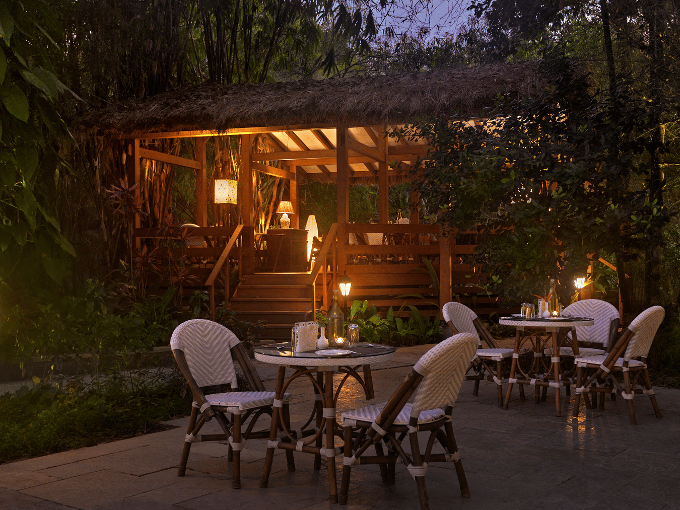 Night view of an outdoor dining area with chairs around tables and a cabin in the background.