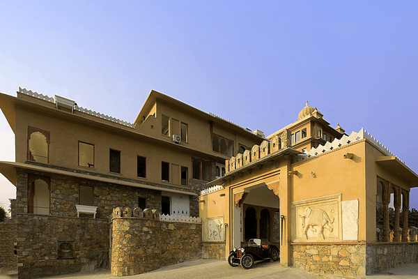 Vintage car parked under the entrance arch at Fateh Garh, Udaipur, flanked by carved elephant relief panels