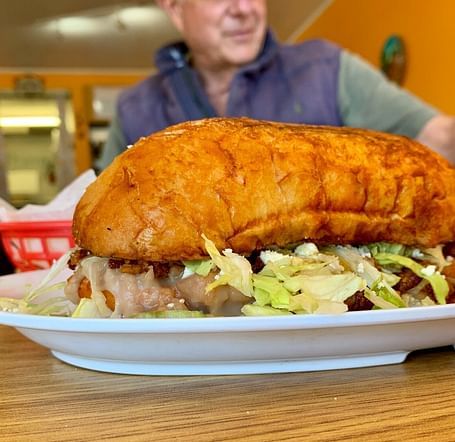 A big burger on a plate with a man in the back