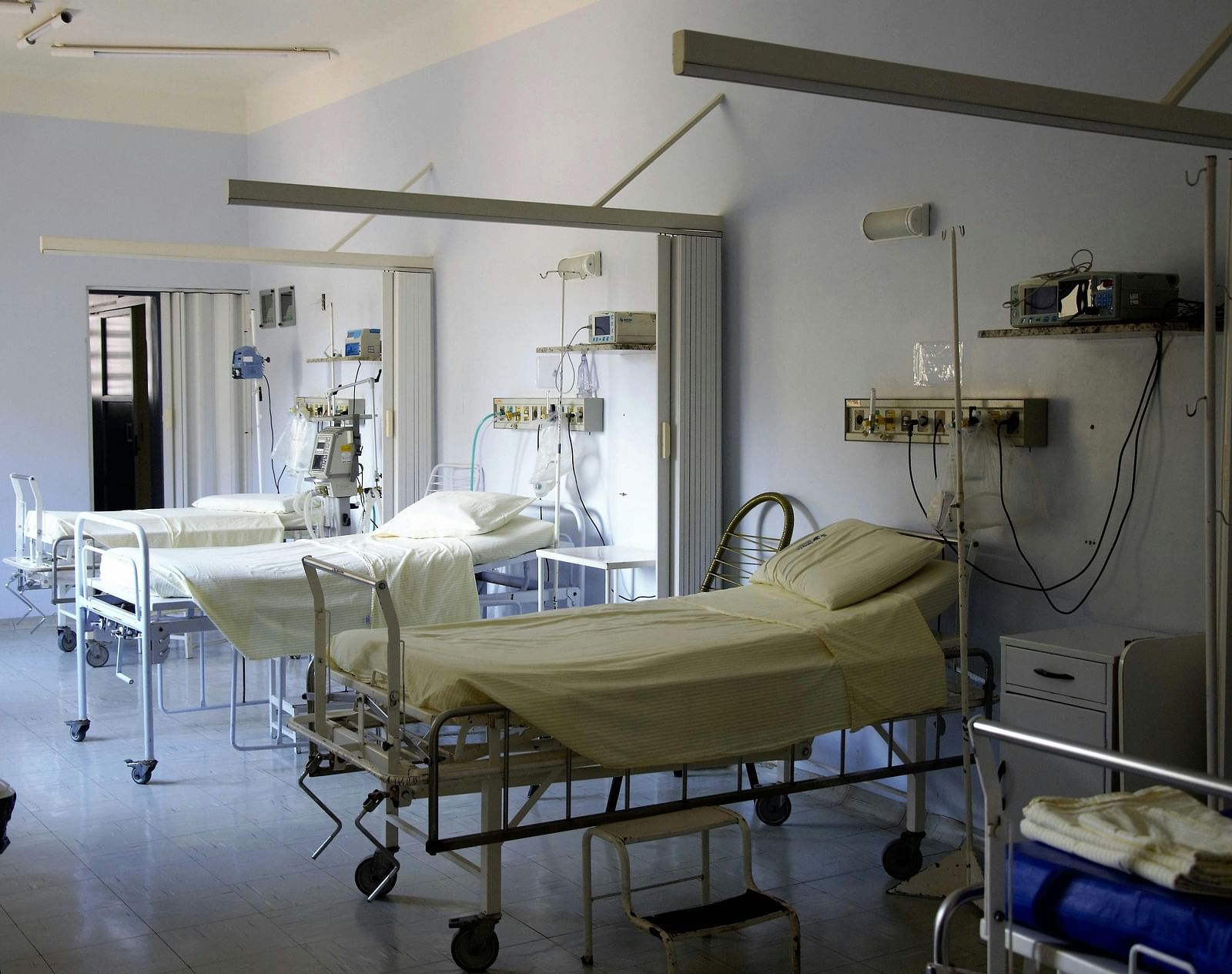A hospital room with empty beds, medical equipment, and white curtains.