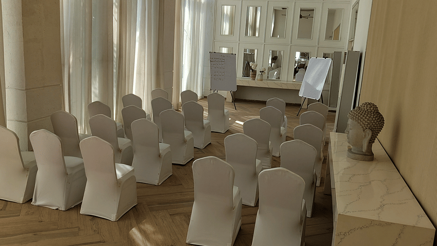 The Mansion House resort conference room with rows of white-covered chairs arranged theater-style facing mirrored wall, prepared for presentations or lectures in a formal setting.