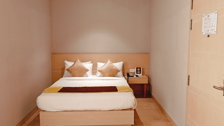 Bedroom view from the entrance of the Business Class Room at Chola Dynasty, Kumbakonam featuring a neatly arranged bed, warm lighting, and a simple yet elegant interior design.
