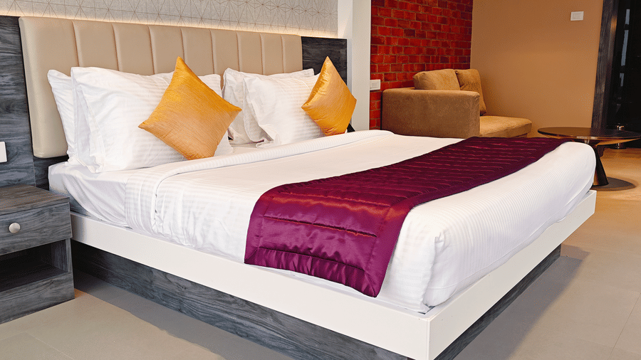 A large bed with a purple runner is shown alongside a beige sofa in a spacious room at Bliss Casa Mila By Bergamont Hotels, Kodaikanal.