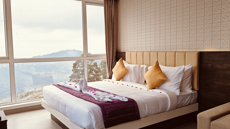 A double bed with white linens and yellow pillows positioned next to a window with a hill view at Bliss Casa Mila By Bergamont Hotels, Kodaikanal.