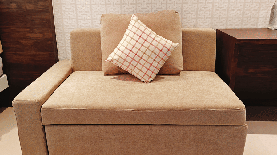 A close-up of a brown fabric sofa bed with 1 patterned cushion placed against a wall at Bliss Casa Mila By Bergamont Hotels, Kodaikanal.
