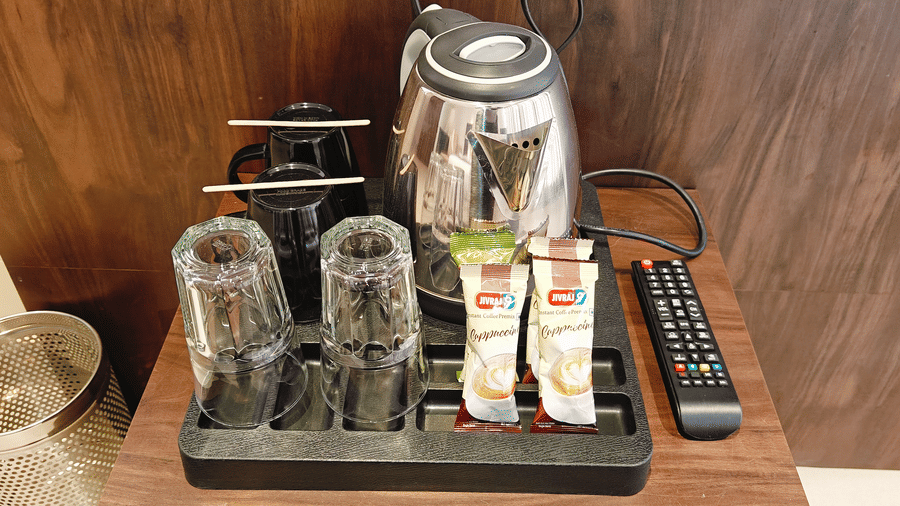 A wooden tray holding 1 silver electric kettle, 2 glass mugs, 2 coffee sachets, and 1 remote at Bliss Casa Mila By Bergamont Hotels, Kodaikanal.