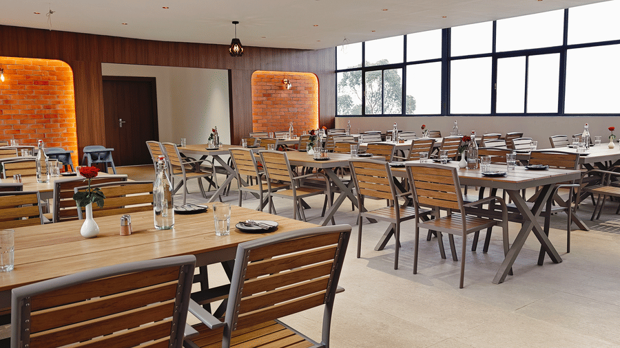 An indoor dining room featuring several wooden tables and chairs arranged neatly under warm lighting at Bliss Casa Mila By Bergamont Hotels, Kodaikanal.