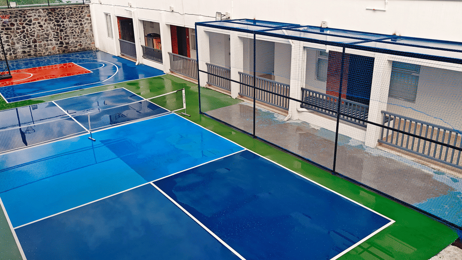 A wide shot of 2 blue and green outdoor courts with a basketball hoop in the background at Bliss Casa Mila By Bergamont Hotels, Kodaikanal.