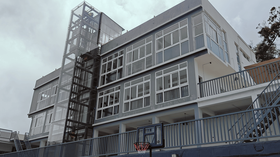 Low angle view of a white multi-storey building with large windows and an external lift at Bliss Casa Mila By Bergamont Hotels, Kodaikanal.