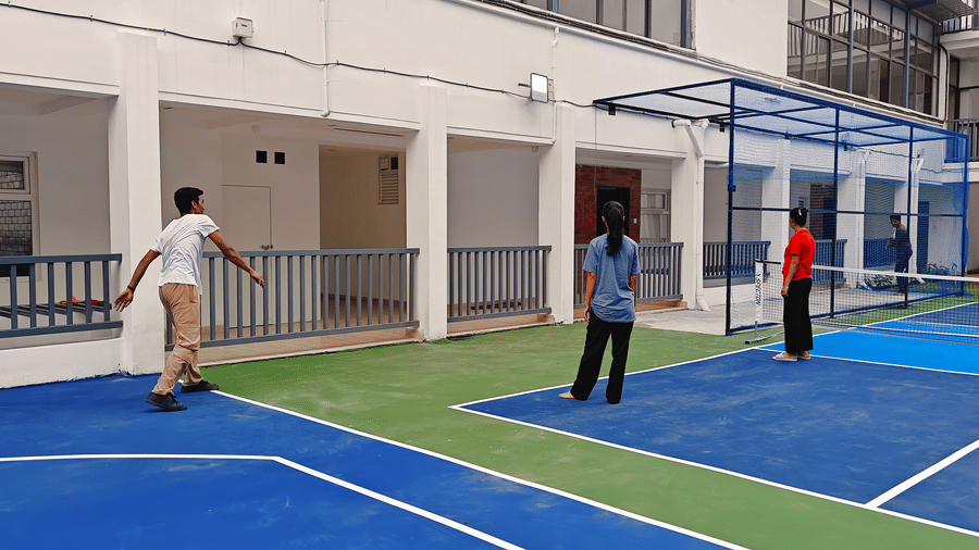 Players positioned on 2 blue outdoor sports courts in front of a white building at Bliss Casa Mila By Bergamont Hotels, Kodaikanal.