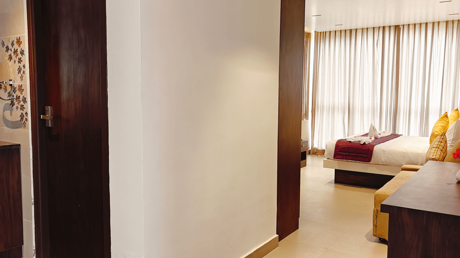 A view from a hallway showing a bathroom door and a glimpse of a bedroom with a double bed at Bliss Casa Mila By Bergamont Hotels, Kodaikanal.