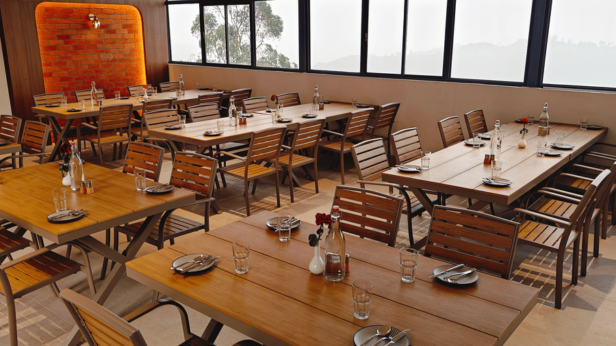 Rectangular wooden tables with matching chairs are set for dining in a room at Bliss Casa Mila By Bergamont Hotels, Kodaikanal.