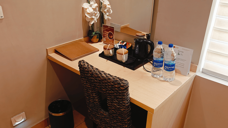 Study desk with in-room amenities in the Business Class Room at Chola Dynasty, Kumbakonam offering a practical workspace, comfortable seating, beverage setup, and a neatly organised corner for guests.