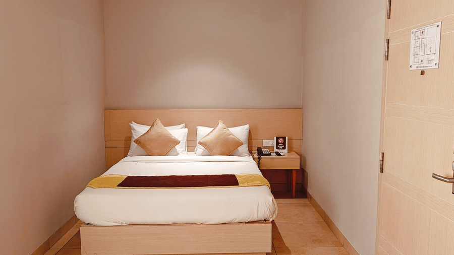 Bedroom view from the entrance of the Business Class Room at Chola Dynasty, Kumbakonam featuring a neatly arranged bed, warm lighting, and a simple yet elegant interior design.