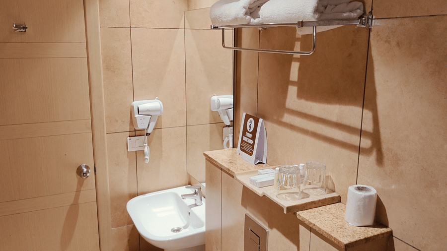 Well-maintained bathroom space at Cholaa Dynasty, Kumbakonam featuring tiled walls, modern fittings, wash basin, and essential toiletries as part of the Deluxe Double Room for a comfortable and hassle-free stay