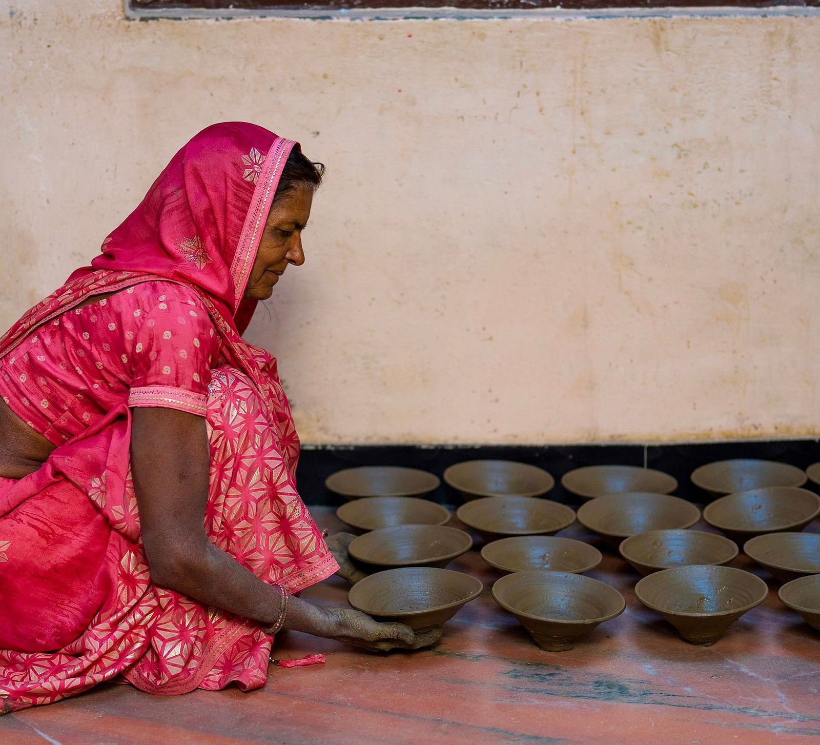 image of a woman draped in a pink saree lining up clay bowls on the floor