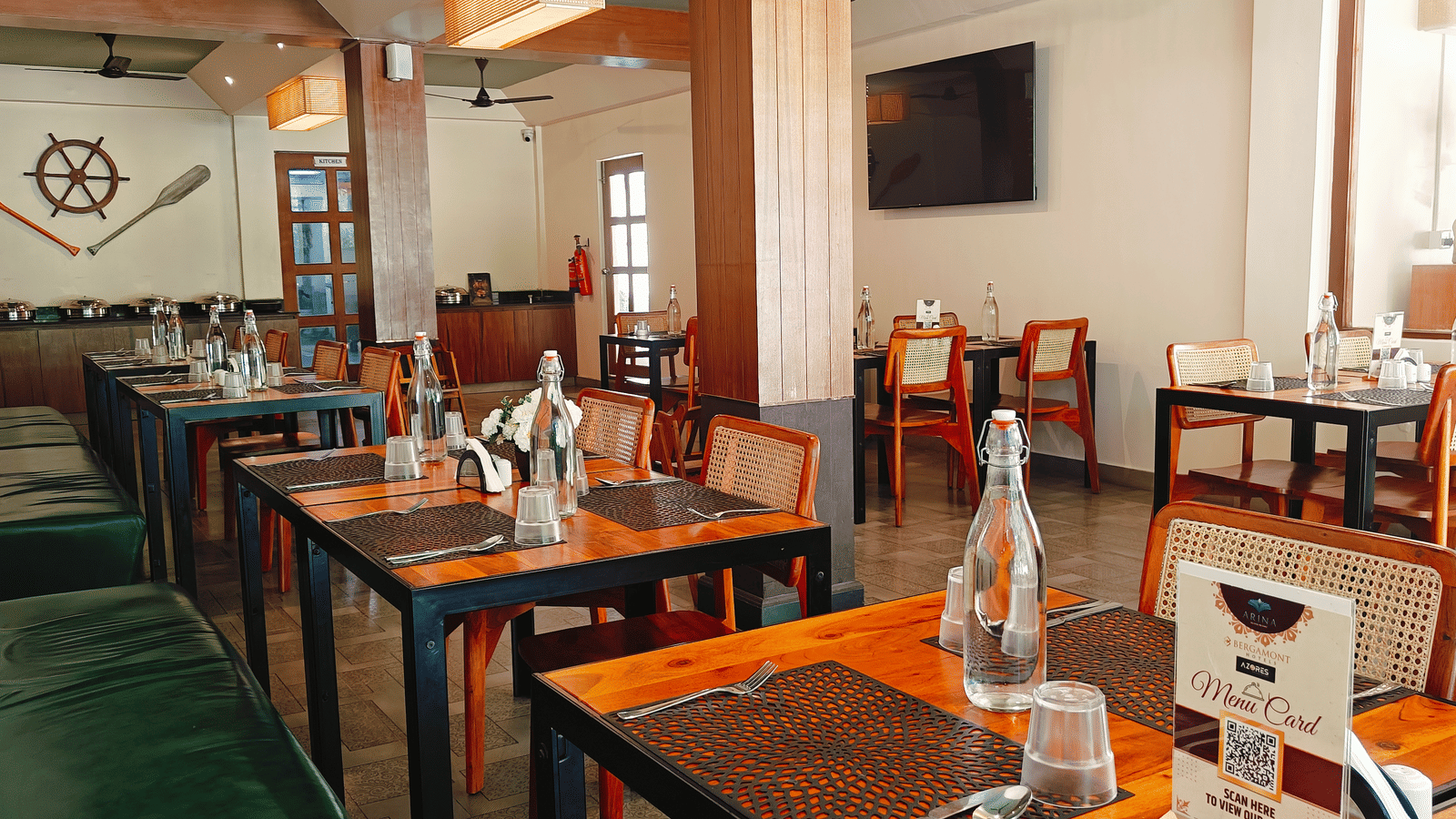 An indoor dining area at Arina Island Resort featuring neatly arranged wooden tables, cushioned seating, and nautical-themed wall decor