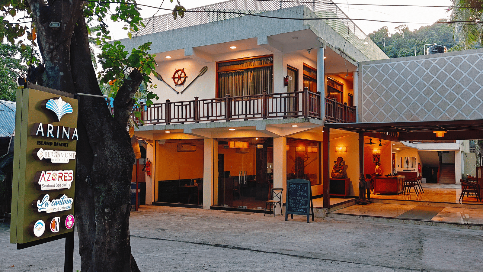 A front view of Arina Island Resort showcasing the main entrance, outdoor seating area, and resort signage near the driveway