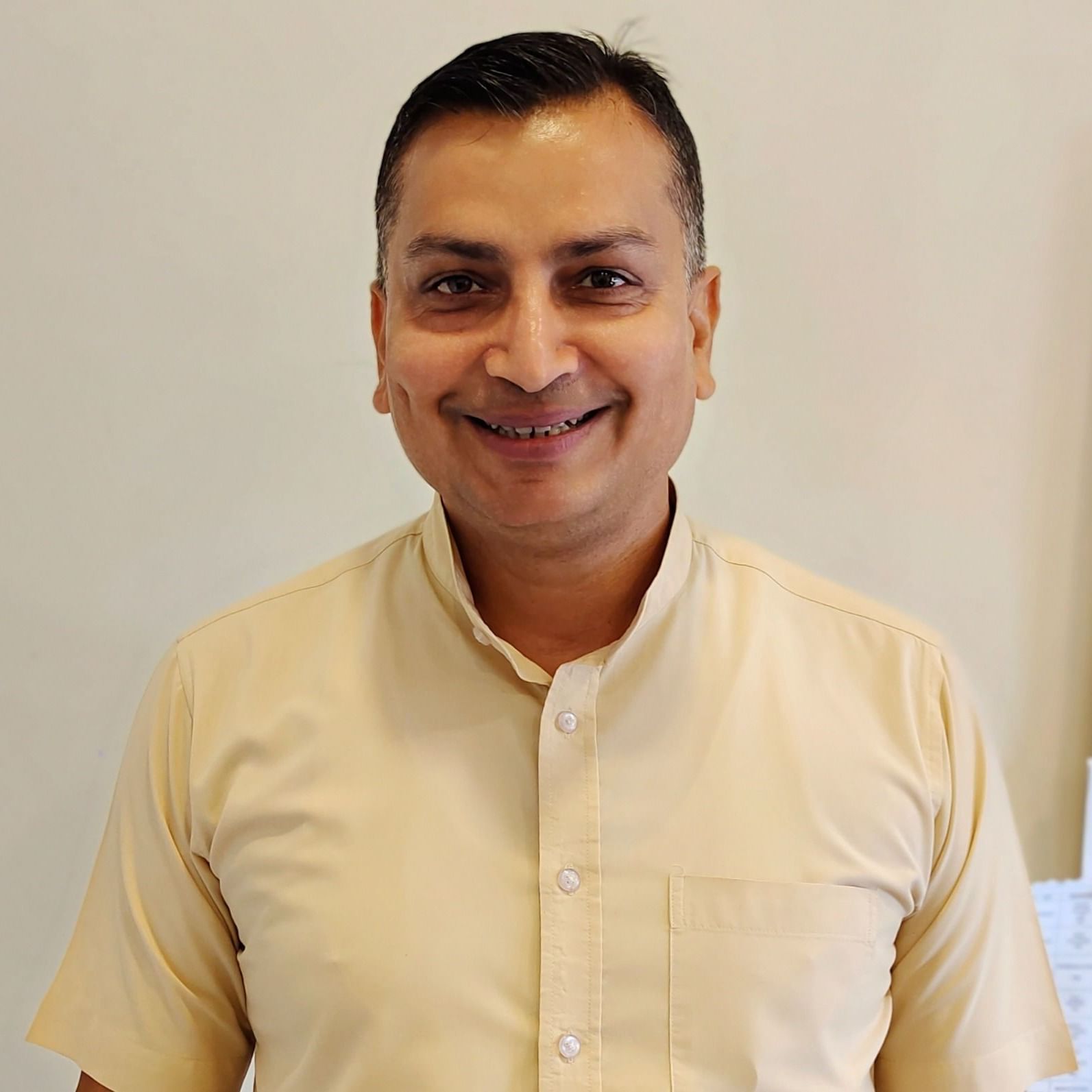 A man with a short haircut and a light-coloured collared shirt smiles widely at the camera