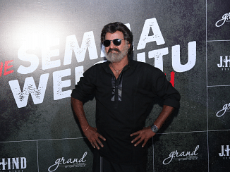 Celebrity posing at an event with a backdrop featuring branding and text.