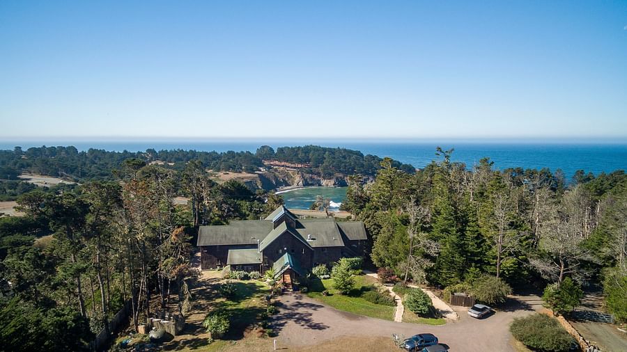 An aerial view of a hotel covered in lush green trees with the Mendocino coast in the background - Brewery Gulch Inn & Spa