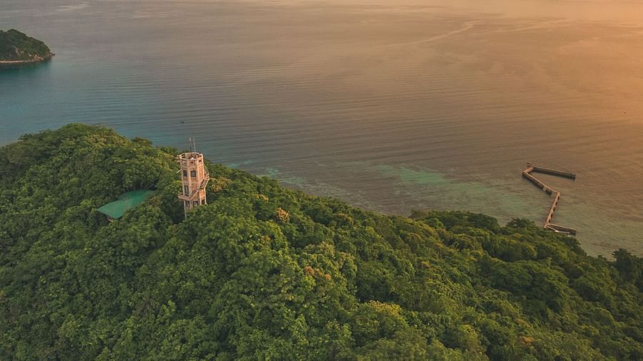 Aerial view of a green hill with a white tower and sea in the background at Flower Island Resort.