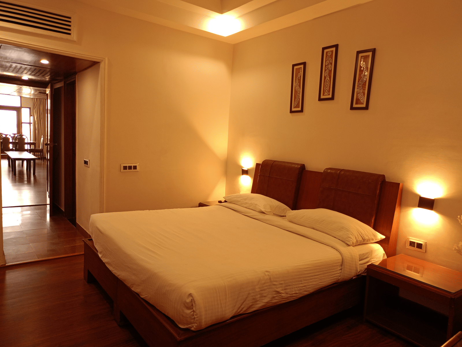 Guest room at Hotel Gold, Panipat featuring a bed, side tables, and framed wall art.
