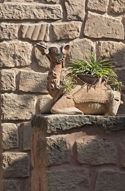 A close up shot of a decorative camel piece place on top of a wall with a plant planted in it - MANVAR Resort & Desert Camp
