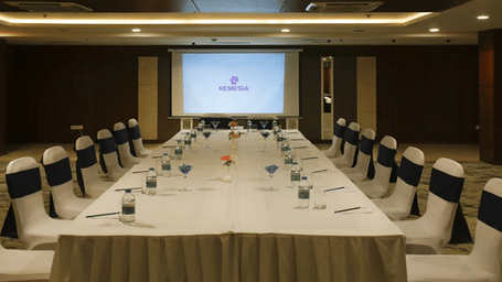 Corporate boardroom meeting setup with a long table, chairs, and projector screen.