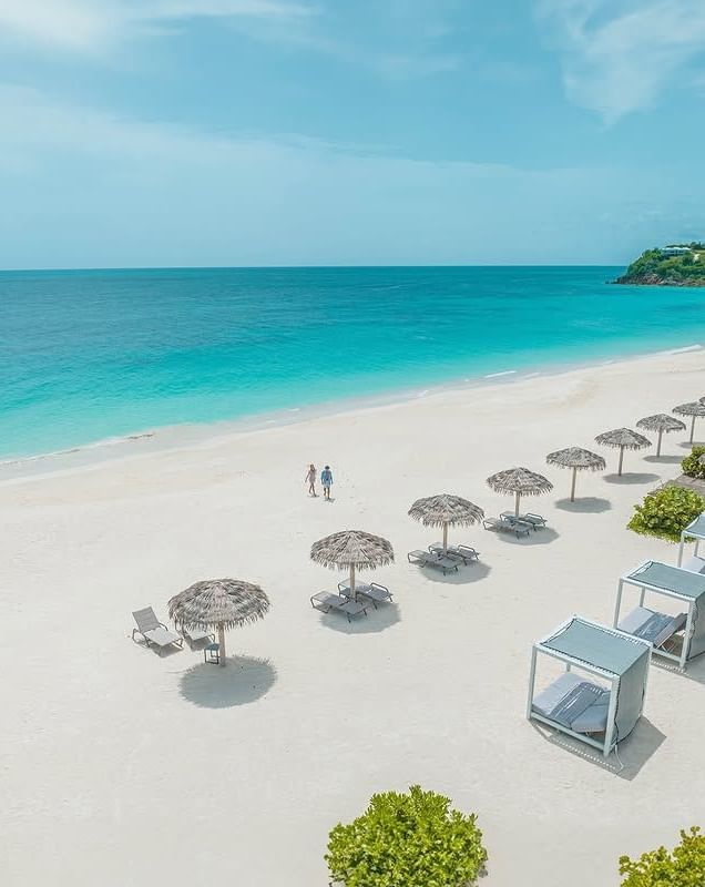 A pristine white sand beach with several thatched umbrellas and cabanas by the turquoise sea - Tamarind Hills Resort and Villas - Antigua