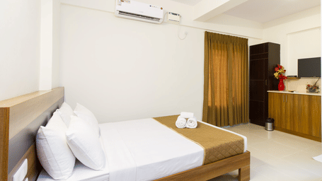 A neatly arranged hotel bedroom with a double bed, dark wood furniture, white walls, and a ceiling fan