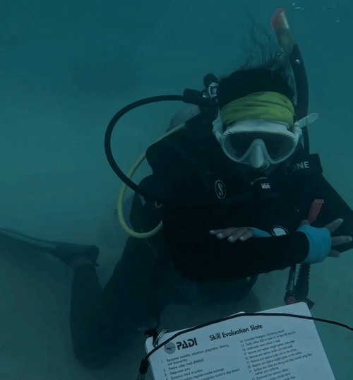 Scuba diver underwater holding a clipboard or slate, completing a written exercise as part of training