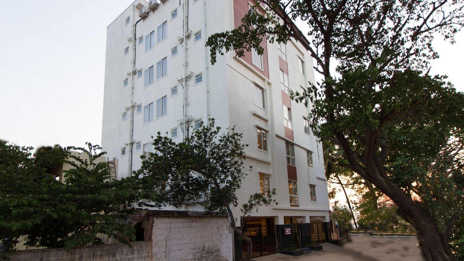The multi-storey building of Sanctum Suites Whitefield, Bangalore amongst trees under a daytime sky.