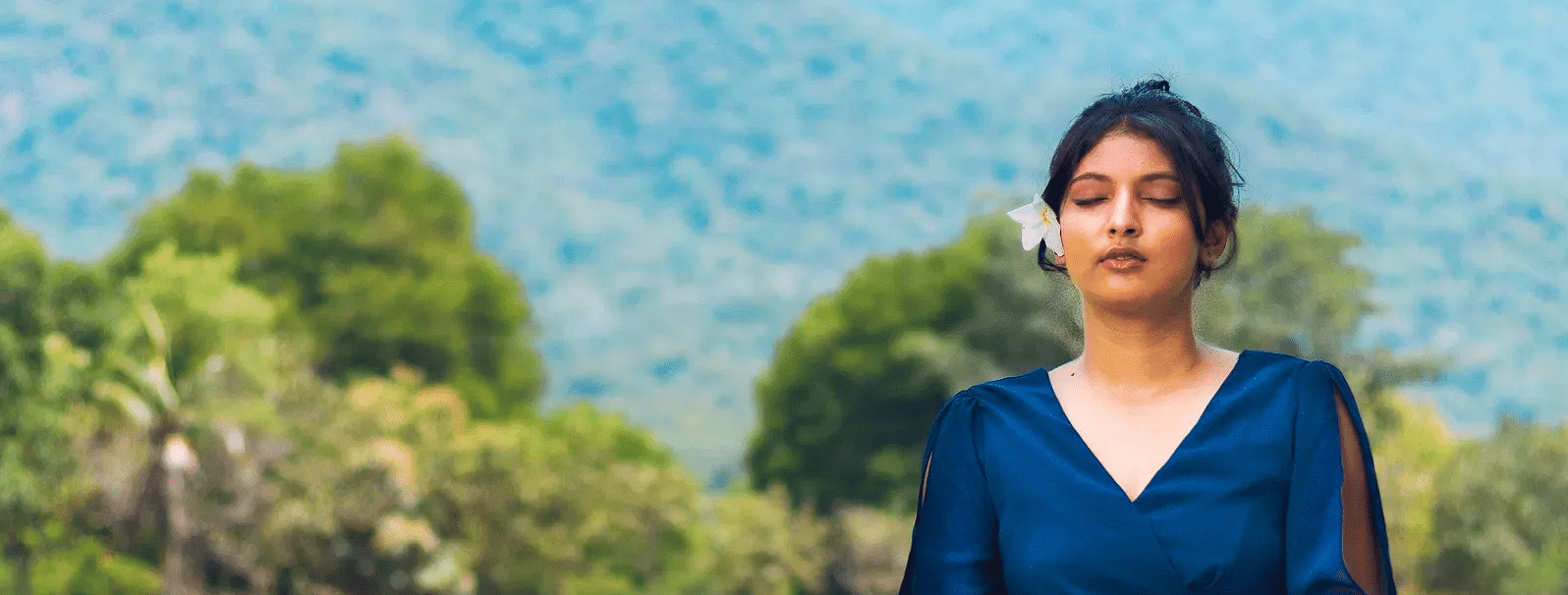 A lady sitting on a mat, doing meditation with a luscious greenery scene behind near Avana resort