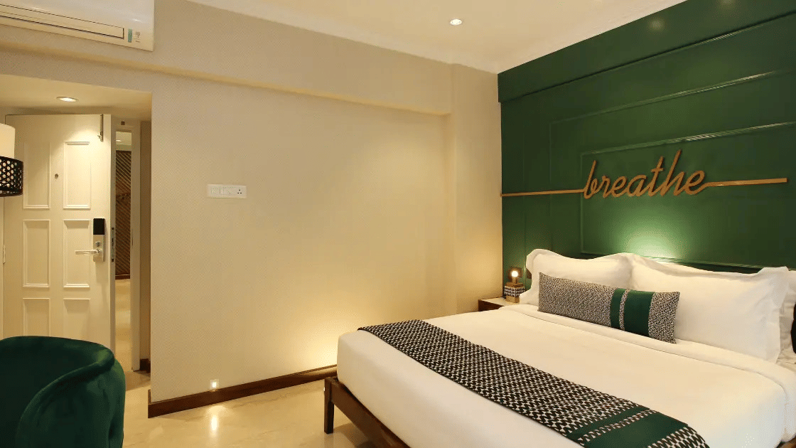 Hotel guest room with green accent wall and neatly made bed