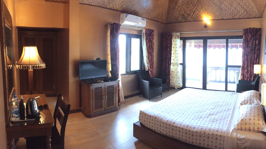 Spacious bedroom with queen size bed, wooden flooring, side lamps, and large windows with sheer curtains at Paradise Lagoon Resort, Udupi.