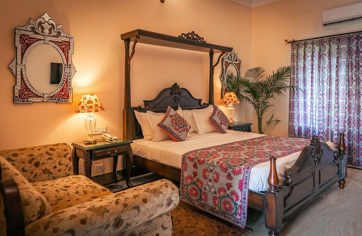 A Deluxe Room with a four-poster bed, a window, a sofa, and elegant decor with warm lighting - Khas Bagh, Jaipur