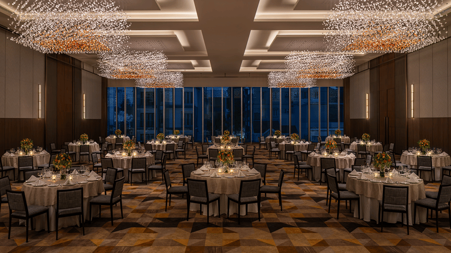 The elegant banquet hall of Ballroom 1 set with round dinner tables and warm overhead lighting against dark glass windows at The Residency Towers Chennai.