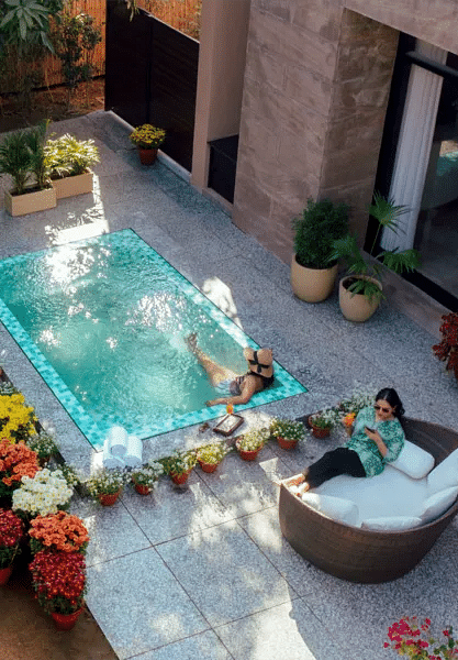 Outdoor hot tub surrounded by plants and seating, placed on a private stone patio with flower pots at Karma Chalets.