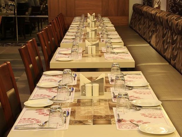 A long dining table set with fine cutlery and napkins, perfect for group dining and special occasions. - Dhanalakshmi Srinivasan Hotels, Perambalur