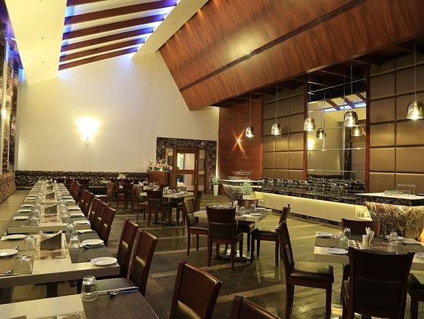A spacious restaurant with elegant wooden interiors, neatly arranged tables, and a warm ambient lighting design. - Dhanalakshmi Srinivasan Hotels, Perambalur